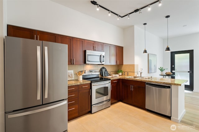 kitchen with a peninsula, rail lighting, a sink, appliances with stainless steel finishes, and backsplash