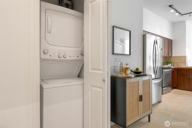 clothes washing area with laundry area, rail lighting, stacked washer / dryer, and a dry bar