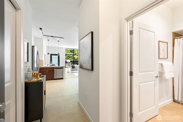 hallway featuring track lighting, baseboards, and light tile patterned floors