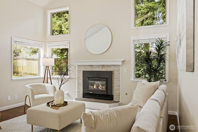 living area featuring wood finished floors, high vaulted ceiling, baseboards, and a tile fireplace