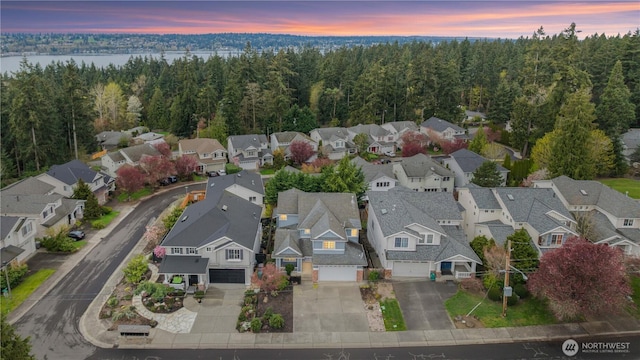 aerial view at dusk featuring a wooded view, a residential view, and a water view