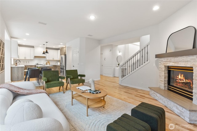 living area featuring a stone fireplace, light wood-style flooring, recessed lighting, and baseboards