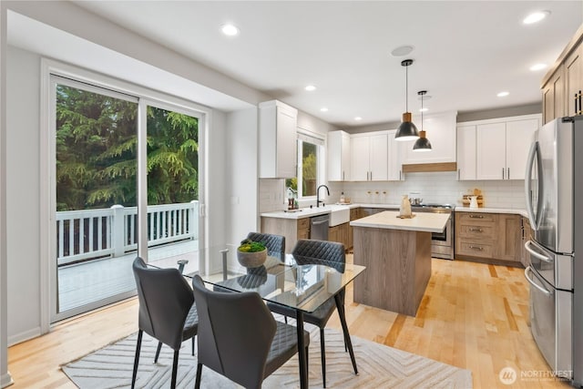 kitchen with light wood-style flooring, light countertops, a kitchen island, decorative backsplash, and stainless steel appliances