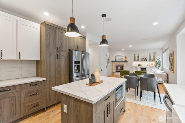 kitchen with a stone fireplace, open floor plan, light wood-style flooring, decorative backsplash, and stainless steel appliances