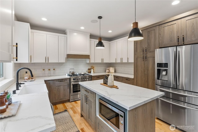 kitchen featuring custom range hood, light wood-style flooring, decorative backsplash, stainless steel appliances, and a sink