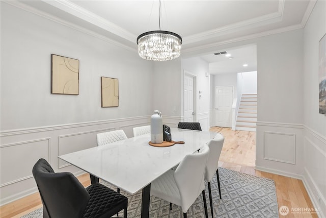 dining space with a notable chandelier, stairs, visible vents, a raised ceiling, and light wood finished floors