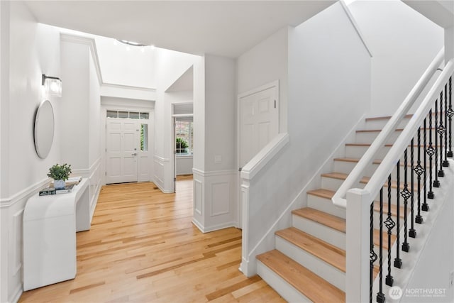 entrance foyer with a decorative wall, light wood finished floors, wainscoting, and stairs