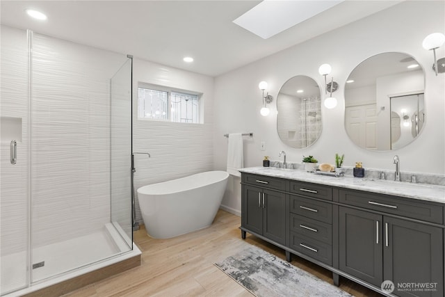 full bathroom with a sink, a skylight, a shower stall, and wood finished floors