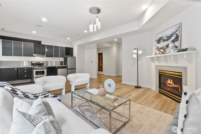 living room with baseboards, recessed lighting, a tile fireplace, and light wood-style floors
