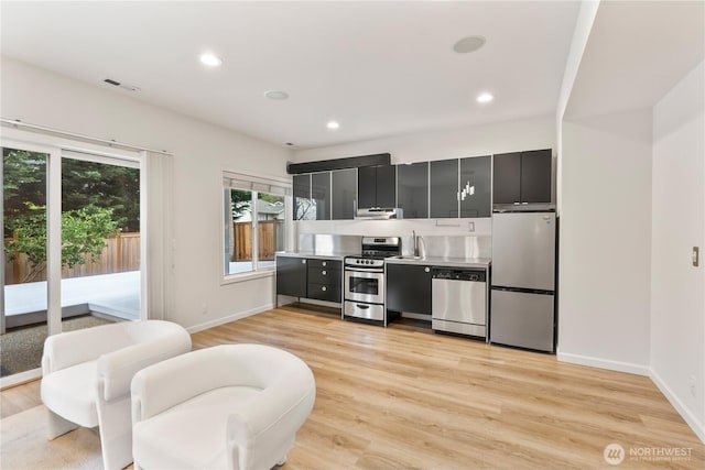 kitchen featuring dark cabinetry, appliances with stainless steel finishes, light wood finished floors, and visible vents
