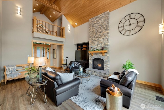 living room featuring wood finished floors, high vaulted ceiling, baseboards, wood ceiling, and a stone fireplace