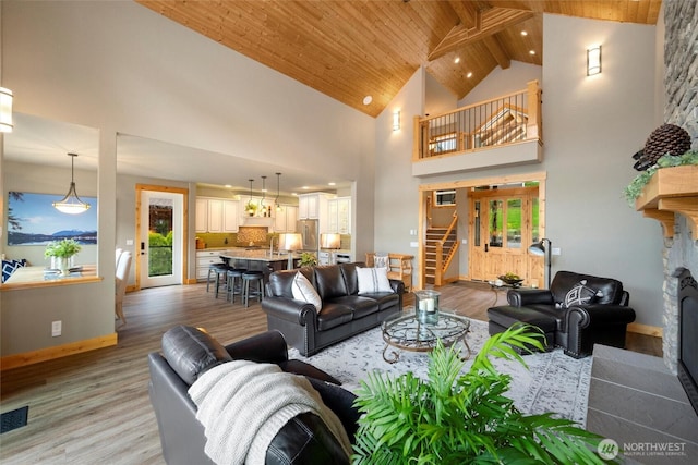 living room featuring stairs, high vaulted ceiling, light wood-style flooring, wooden ceiling, and a fireplace