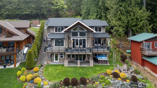 back of property featuring an outdoor hot tub, a patio area, a shingled roof, and a yard
