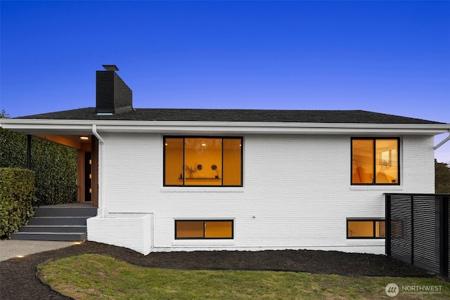 view of side of property with brick siding, fence, a chimney, and a shingled roof