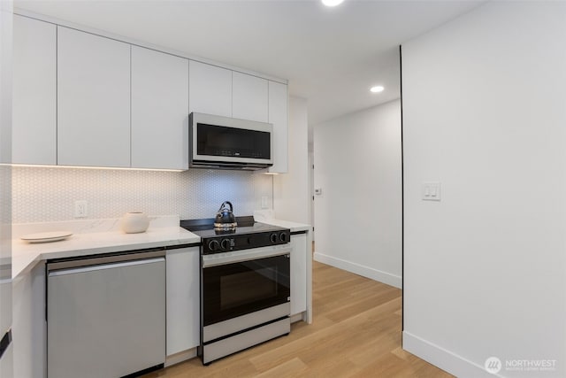 kitchen featuring light wood-type flooring, light countertops, stainless steel microwave, white cabinets, and electric stove