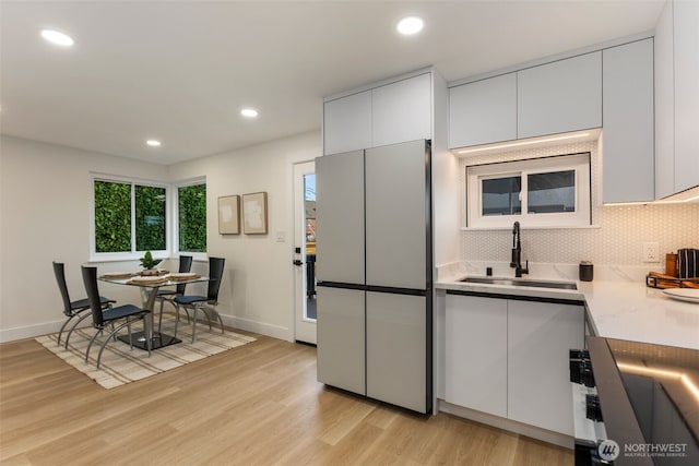 kitchen with white cabinets, a sink, light countertops, light wood-style flooring, and decorative backsplash