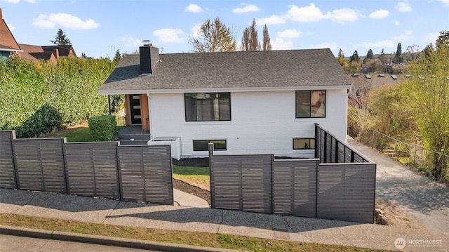 view of front of property featuring brick siding, a shingled roof, a chimney, and fence private yard