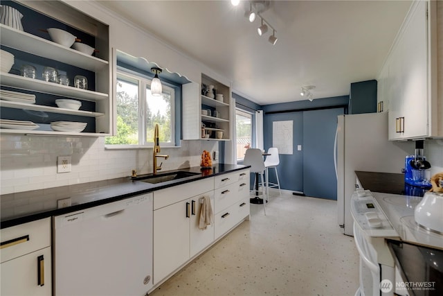 kitchen featuring white dishwasher, open shelves, dark countertops, a sink, and tasteful backsplash
