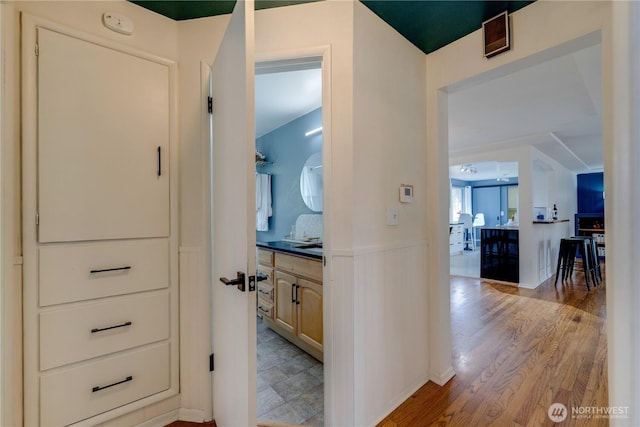 corridor with light wood finished floors and a wainscoted wall