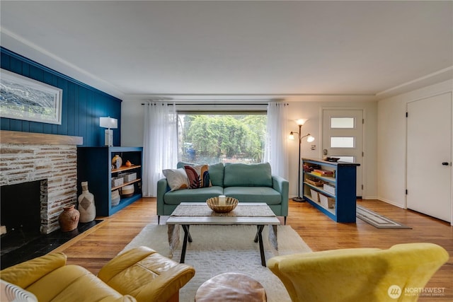 living area featuring ornamental molding, a stone fireplace, and wood finished floors