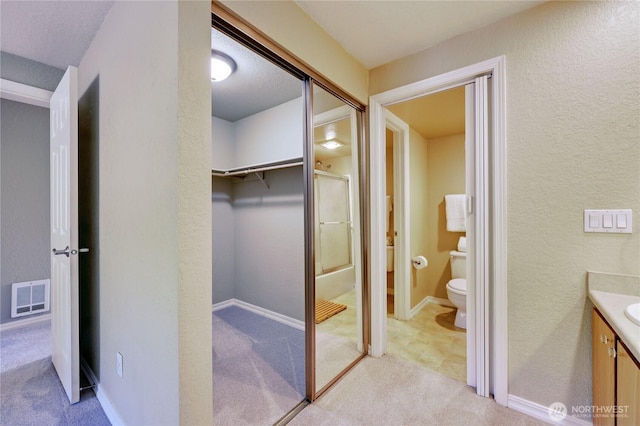 bathroom with a walk in closet, vanity, toilet, an enclosed shower, and visible vents