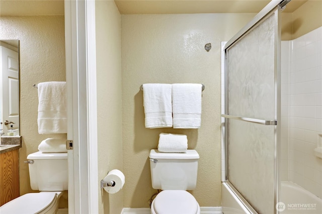 bathroom with vanity, a textured wall, toilet, and shower / bath combination with glass door
