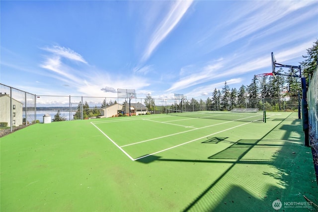 view of tennis court featuring a water view and fence