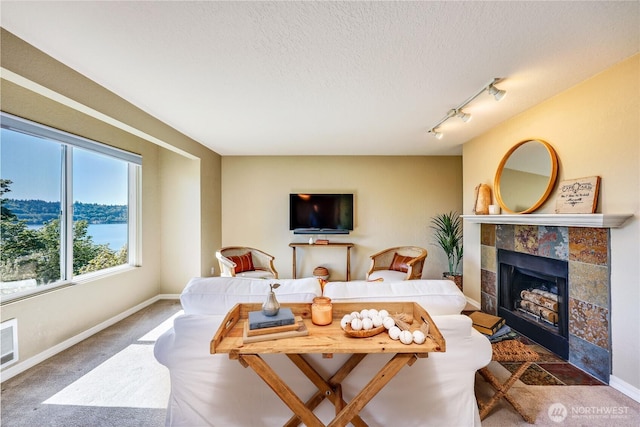 living room with carpet floors, a textured ceiling, baseboards, and a tile fireplace