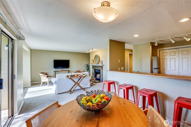dining space featuring carpet flooring, a textured ceiling, rail lighting, a tiled fireplace, and recessed lighting