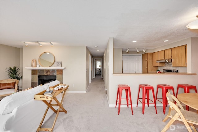 interior space featuring under cabinet range hood, rail lighting, light colored carpet, and a kitchen bar