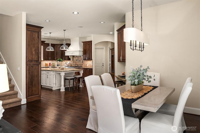 dining space with recessed lighting, arched walkways, baseboards, stairway, and dark wood-type flooring