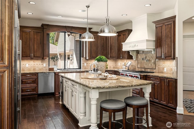 kitchen with stainless steel appliances, a sink, a center island, dark wood-type flooring, and premium range hood