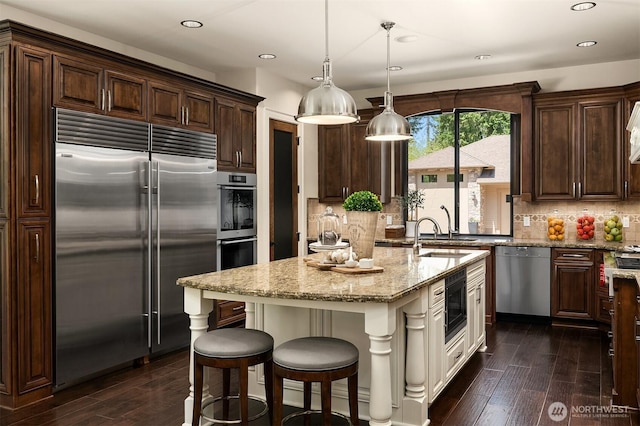 kitchen with light stone counters, a sink, built in appliances, dark wood-style floors, and recessed lighting