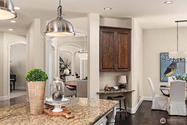 interior space with baseboards, decorative columns, arched walkways, and dark brown cabinetry