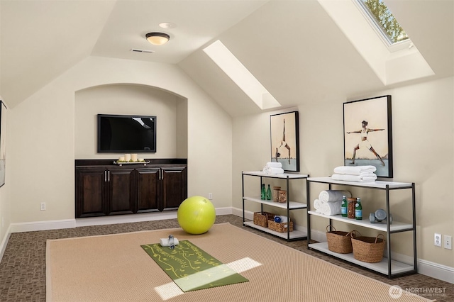 exercise room featuring baseboards, visible vents, vaulted ceiling with skylight, and carpet