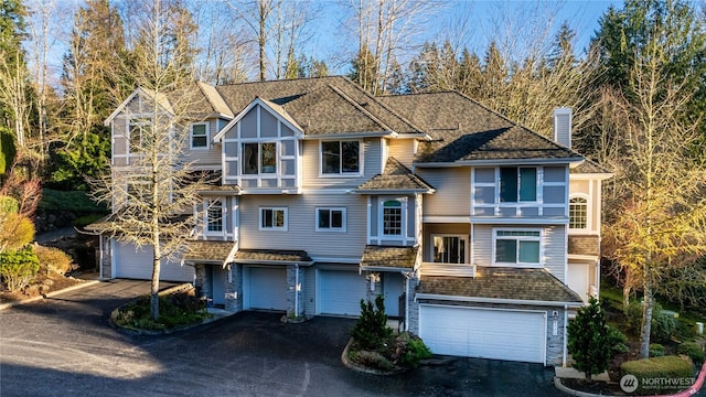 view of front of property featuring roof with shingles, an attached garage, driveway, and a chimney