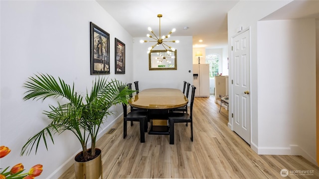 dining room featuring light wood-style floors, a notable chandelier, baseboards, and visible vents