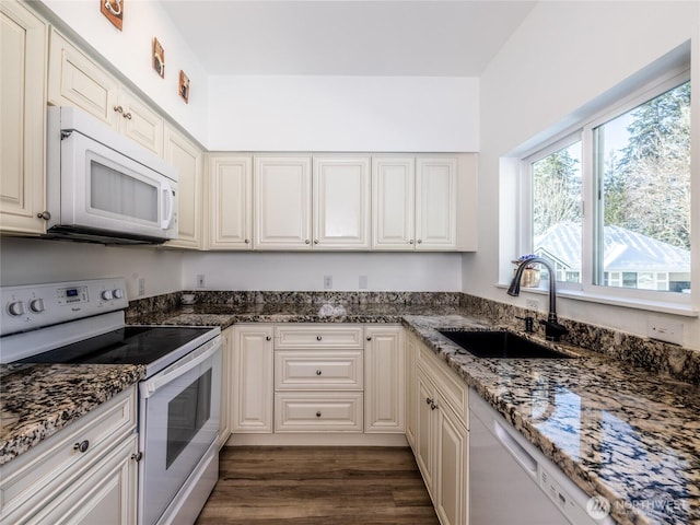 kitchen with white appliances, white cabinetry, dark stone counters, dark wood finished floors, and a sink