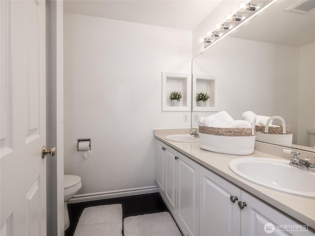 bathroom featuring visible vents, toilet, a sink, double vanity, and baseboards