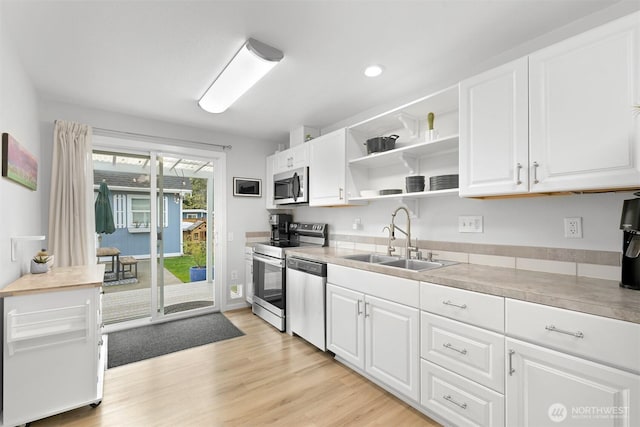 kitchen with appliances with stainless steel finishes, light wood finished floors, a sink, and white cabinetry