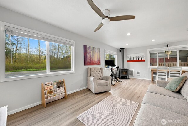 living room featuring wood finished floors, ceiling fan, baseboards, and a wood stove