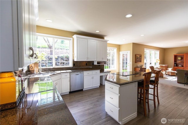 kitchen featuring dishwasher, a sink, dark countertops, a kitchen bar, and wood finished floors