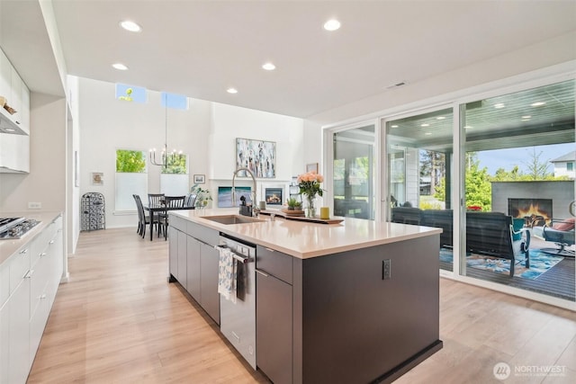 kitchen with a glass covered fireplace, a sink, stainless steel appliances, light wood-type flooring, and recessed lighting