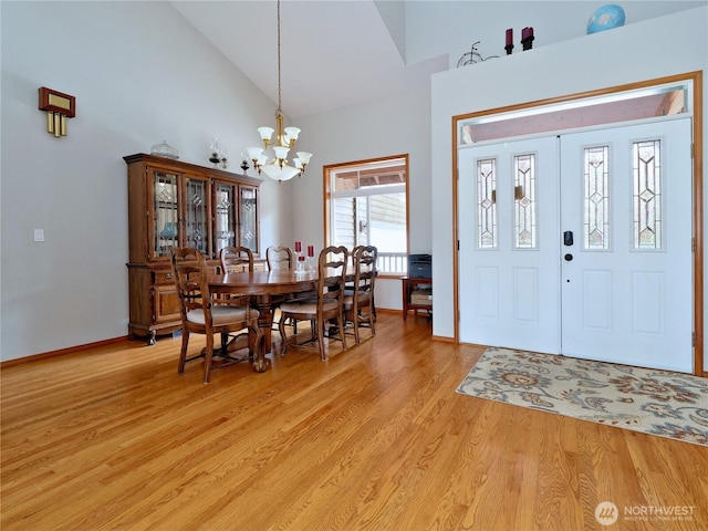 entryway featuring light wood-style floors, high vaulted ceiling, a notable chandelier, and baseboards