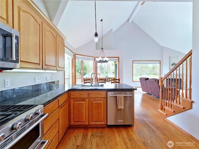 kitchen featuring light wood-style floors, a peninsula, a sink, stainless steel appliances, and beam ceiling