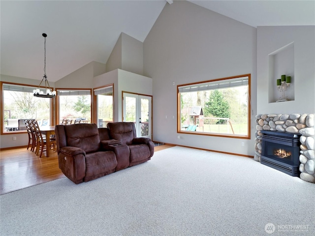 carpeted living area with baseboards, an inviting chandelier, a fireplace, french doors, and high vaulted ceiling