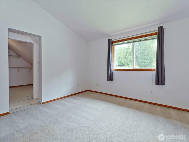 spare room with carpet flooring, baseboards, and lofted ceiling