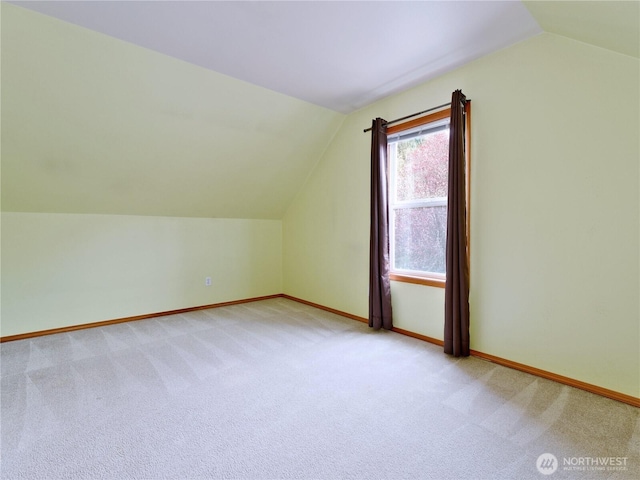 additional living space with baseboards, light colored carpet, and vaulted ceiling