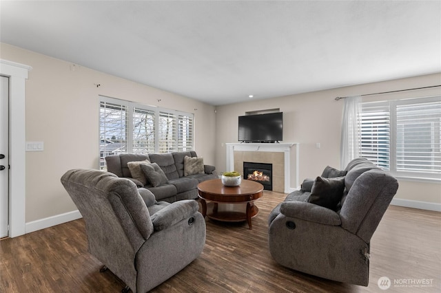 living area featuring a tiled fireplace, baseboards, and wood finished floors