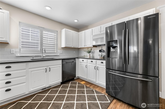kitchen featuring white microwave, stainless steel fridge with ice dispenser, dishwasher, a sink, and dark countertops
